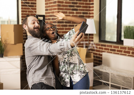 Caucasian man holds cellphone while attending online call with African American girlfriend, sharing updates with family. Happy multiethnic couple warmly greeting loved ones during video conference. 136137612