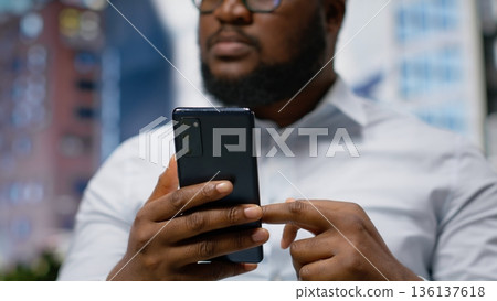 Adult man moves through metropolitan sidewalk with confidence, checking his navigation and gps on smartphone. Modern city life attitude while walking on pavement downtown. Camera B. 136137618