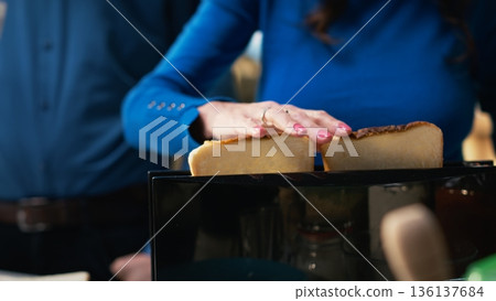 Retired couple preparing breakfast with toast from the toaster, standing together by the countertop. Man and woman enjoying a moment, chatting and bonding during retired life. Camera B. 136137684