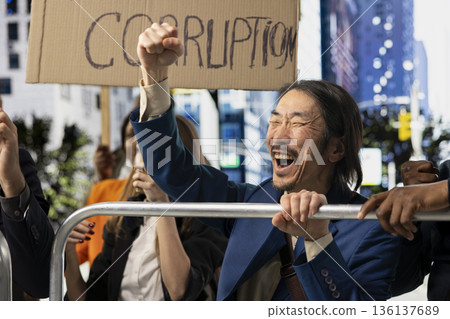 Asian man annoyed screaming at political protest with large protesters crowd, taking action against corrupt government, posters with messages like stop corruption and equal rights. Asian man annoyed screaming at political protest with large protesters crowd, taking action against corrupt government, posters with messages like stop corruption and equal rights. 136137689
