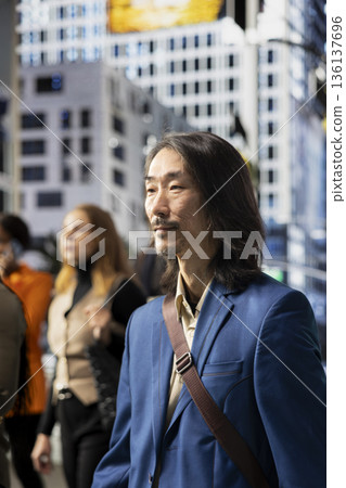 Asian businessman crossing street near diverse pedestrians crowd during commute on the way to the office. Mix of adults, business people and active population navigating the city life. Asian businessman crossing street near diverse pedestrians crowd during commute on the way to the office. Mix of adults, business people and active population navigating the city life. 136137696