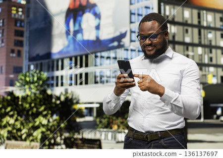 African american male opening navigation on smartphone for downtown walk with casual confidence, street style and vibrant attitude through the architecture of metropolitan area. African american male opening navigation on smartphone for downtown walk with casual confidence, street style and vibrant attitude through the architecture of metropolitan area. 136137697