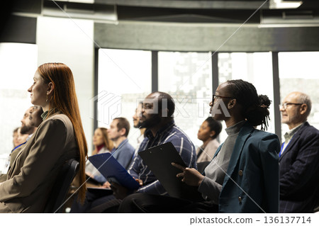 Seated black businessman taking notes on clipboard files from the audience, listening to business presentation for development and training. Participant at international convention summit. Seated black businessman taking notes on clipboard files from the audience, listening to business presentation for development and training. Participant at international convention summit. 136137714