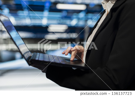 Close up of data center worker using laptop to do maintenance on electronics processing large datasets. Server hub IT expert does backups with notebook to protect gear used by cloud storage companies 136137723