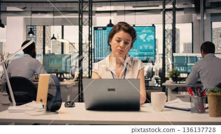 Businesswoman working alone at office desk using laptop, corporate lifestyle. Business intelligence, data analysis dashboard, performance metrics, planning objectives and goals. Businesswoman working alone at office desk using laptop, corporate lifestyle. Business intelligence, data analysis dashboard, performance metrics, planning objectives and goals. 136137728