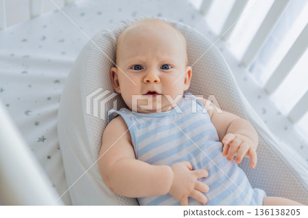 Baby lying peacefully in a cozy cocoon nest inside a crib, feeling safe and calm at home. Soft light and warm atmosphere highlight comfort and care. Infant sleep, safety and gentle parenting concept 136138205