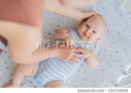 Mother sitting beside the crib gently stroking her baby lying in a cozy bed at home. Warm intimate moment filled with love, trust and calm. Motherhood, infant comfort and emotional bonding concept Mother sitting beside the crib gently stroking her baby lying in a cozy bed at home. Warm intimate moment filled with love, trust and calm. Motherhood, infant comfort and emotional bonding concept 136138208
