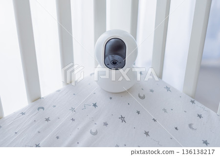 Baby monitor camera placed inside a crib for watching a sleeping infant. Modern parenting solution for safety and peace of mind at home. Childcare technology, baby monitoring and smart parenting Baby monitor camera placed inside a crib for watching a sleeping infant. Modern parenting solution for safety and peace of mind at home. Childcare technology, baby monitoring and smart parenting 136138217