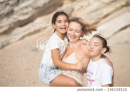 Loving mother embracing daughters on beach in Loving mother embracing daughters on beach in 136138528