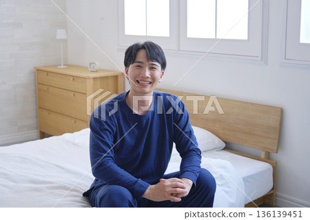 A man in his 20s sitting on a bed, portrait, looking at the camera A man in his 20s sitting on a bed, portrait, looking at the camera 136139451