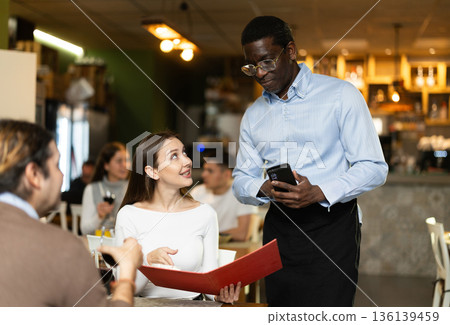Woman, after reading the menu, makes an order from an African waiter 136139459
