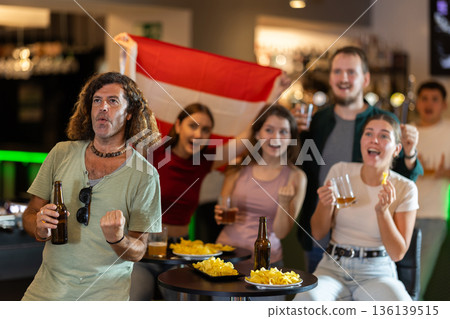 Men and women supporting Austria sports team in pub together. Group of friends raising Austria flag 136139515