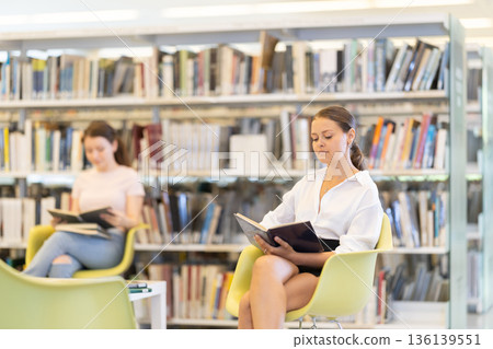 Female sitting on a chair in the library against the background of students 136139551