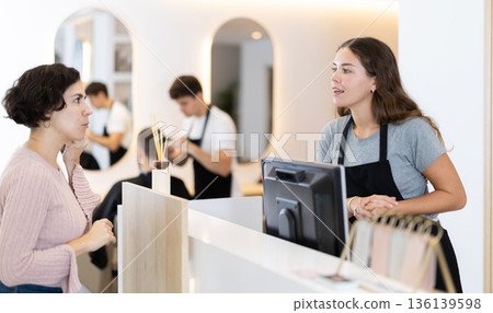Female stylist stands near barbershop reception desk, communicates with female visitor Female stylist stands near barbershop reception desk, communicates with female visitor 136139598