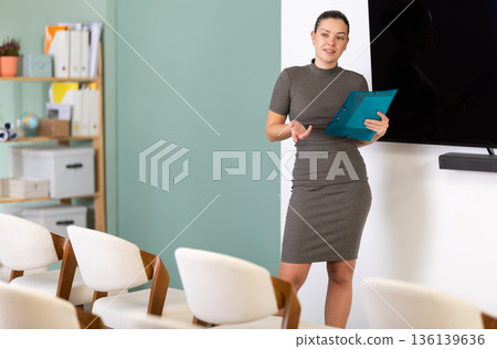 Female coach with folder with papers standing near blackboard in classroom 136139636