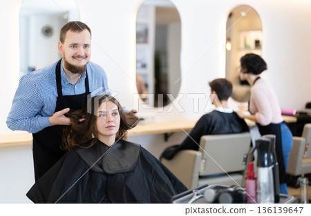 Young man barbershop employee stands next to female client, discussing details of haircut 136139647