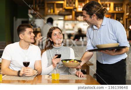 Male waiter brings dishes that the couple ordered 136139648