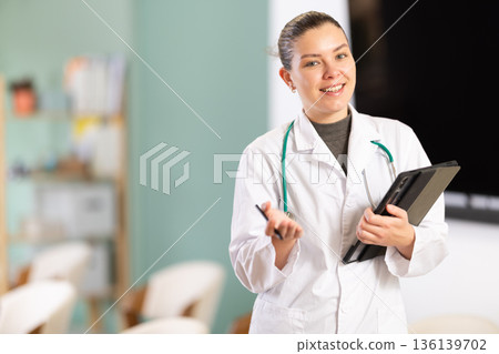 Doctor girl office employee with tablet greets and invite visitors Doctor girl office employee with tablet greets and invite visitors 136139702