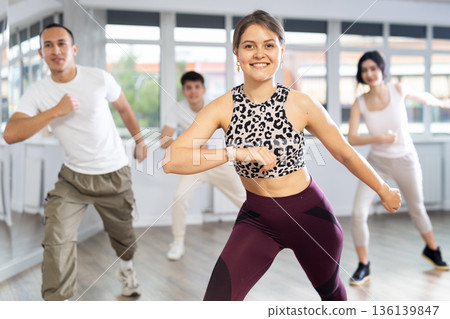 Happy young pretty girl and group of multinational young people practicing new vigorous swing techniques at dance school Happy young pretty girl and group of multinational young people practicing new vigorous swing techniques at dance school 136139847
