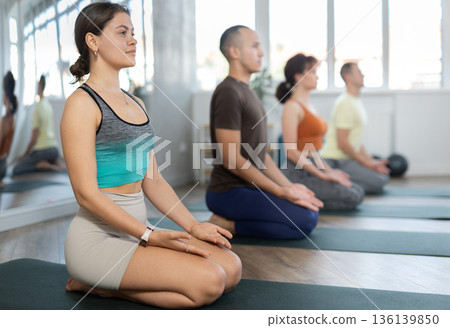 Lovers of active lifestyle on yoga mat perform doing diamond pose, vajrasana in gym Lovers of active lifestyle on yoga mat perform doing diamond pose, vajrasana in gym 136139850