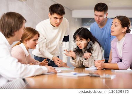 Young teacher discussing his notes with students around the table Young teacher discussing his notes with students around the table 136139875
