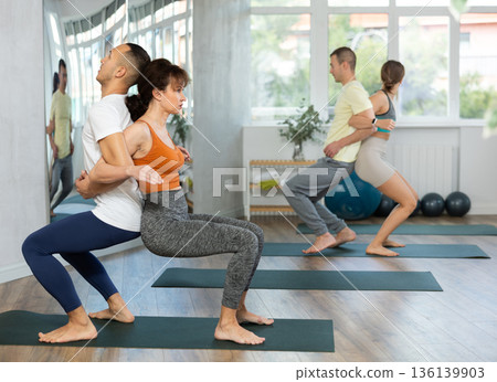 Lovers of active lifestyle perform pair yoga back to back chair pose in gym 136139903