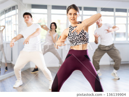 Positive young girl dancing vigorous swing with other people during group training Positive young girl dancing vigorous swing with other people during group training 136139904