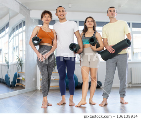 Happy portrait of four young people posing with mats, going to practicing yoga at gym Happy portrait of four young people posing with mats, going to practicing yoga at gym 136139914