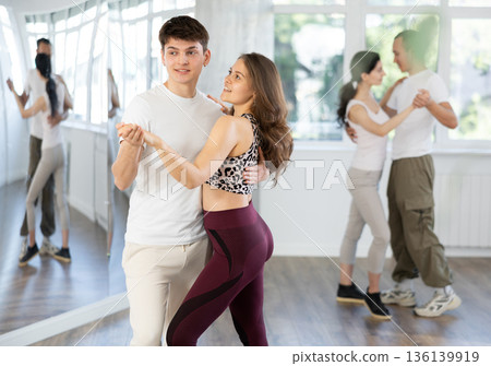 Girl paired up with young man, they train to perform slow waltz dance, rehearse performance. 136139919