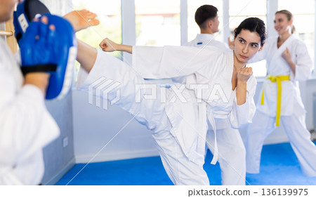 Young girl training kicks on punch mitts held by instructor 136139975
