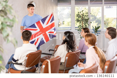Young teacher holding flag of Great Britain in front of group of students 136140111