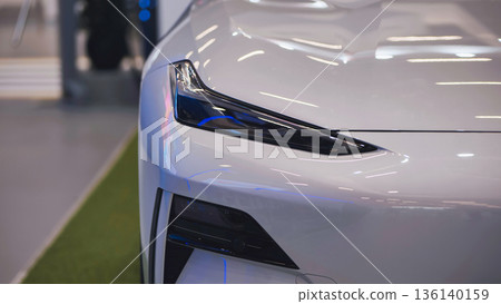 Sleek white electric car showcasing modern headlight design in showroom Sleek white electric car showcasing modern headlight design in showroom 136140159