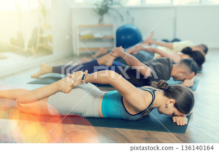 Happy young woman with sports people doing bow pose of yoga on mat together in yoga studio 136140164
