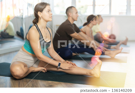 Portrait of woman making stretching legs with multinational group sitting on sports mat and making yoga exercise at fitness club Portrait of woman making stretching legs with multinational group sitting on sports mat and making yoga exercise at fitness club 136140209