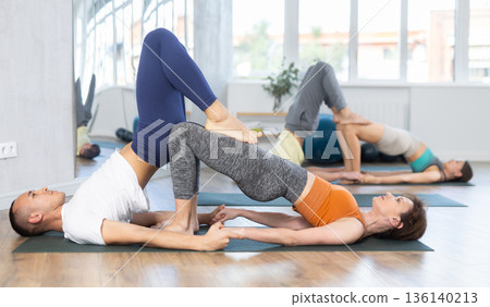 Lovers of active lifestyle perform pair yoga bridge and supported shoulderstand pose in gym Lovers of active lifestyle perform pair yoga bridge and supported shoulderstand pose in gym 136140213