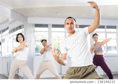 Positive young men and girls dancing modern street dance together during their group training at dance hall Positive young men and girls dancing modern street dance together during their group training at dance hall 136140215