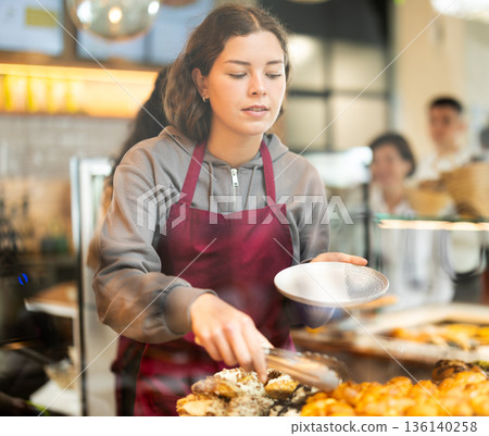 Young woman putting pastries on plate in cafe 136140258