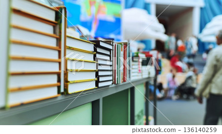 Books stacked on bookstore shelf with blurry people in background 136140259