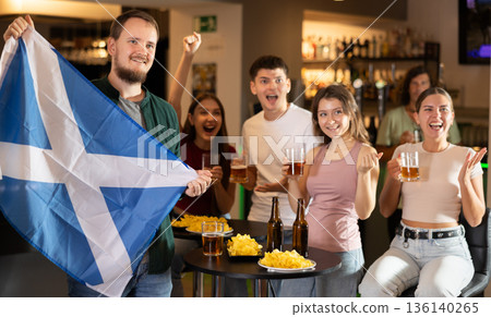Football fans waving the flag of Scotland while drinking beer and watching tournament in sport bar 136140265