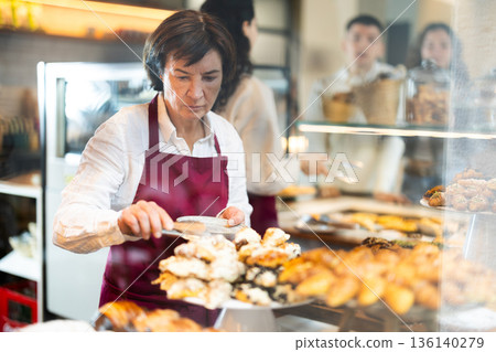 Senior woman salesperson works in cafeteria bakery shop Senior woman salesperson works in cafeteria bakery shop 136140279