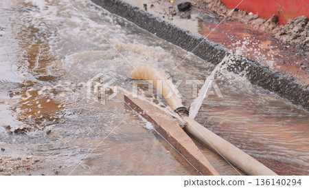 Flooding street with water gushing from a pipe laying on the ground 136140294