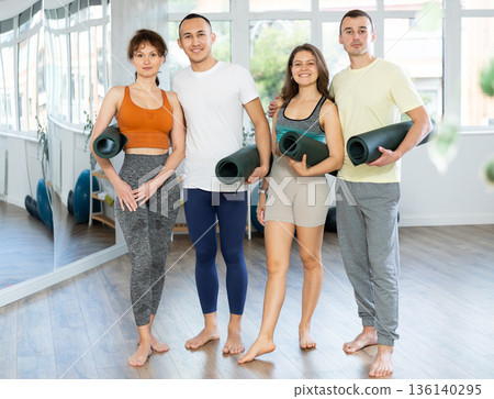 Happy portrait of four young people posing with mats, going to practicing yoga at gym Happy portrait of four young people posing with mats, going to practicing yoga at gym 136140295