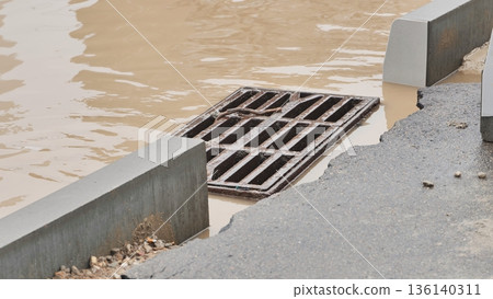 Grate overflowing with muddy stormwater on urban street after heavy rain 136140311