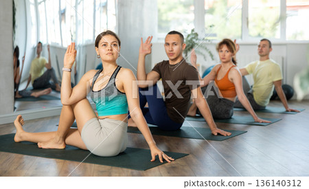 Lovers of active lifestyle on yoga mat perform doing wakrasana, snail pose in gym Lovers of active lifestyle on yoga mat perform doing wakrasana, snail pose in gym 136140312