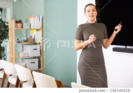 Young woman coach presenting in auditorium with remote control 136140318