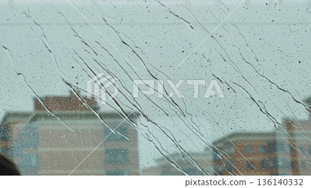 Raindrops running down window, city buildings blurring in background on a wet day 136140332
