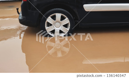 Car driving through flooded urban street splashing muddy water during heavy rain 136140347