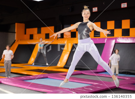 Sportive European female in active wear bouncing and jumping on trampolines in leisure sports center Sportive European female in active wear bouncing and jumping on trampolines in leisure sports center 136140355