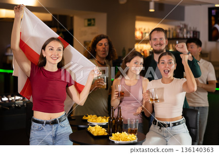 Company of fans of different ages waving flag of England and celebrating victory of favorite team in sports bar 136140363