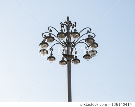 Ornate vintage street lamp with multiple lights against a clear blue sky 136140414